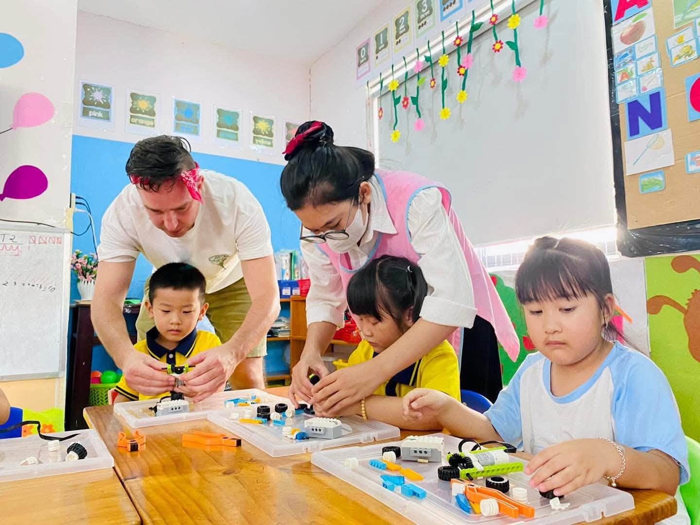 Giáo viên nước ngoài và cô giáo Việt cùng hướng dẫn các bé lắp ráp robot trong lớp học